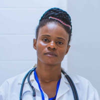 Imagem de uma mulher negra, com cabelo traçado em coque alto, usando um jaleco branco, com um estetoscópio pendurado no pescoço. 